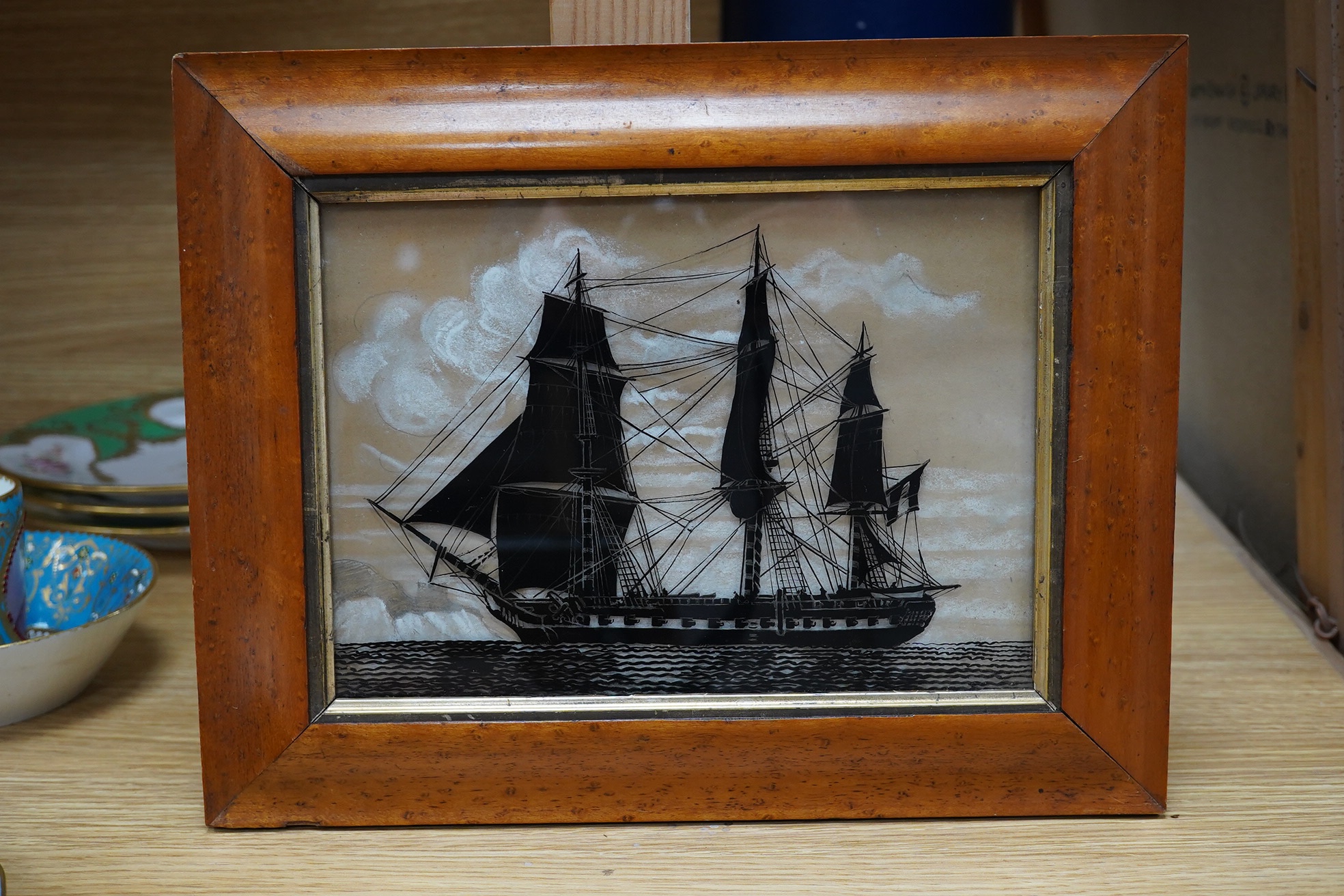 A reverse glass painted silhouette of a sailing ship, unsigned, 15 x 22cm, maple framed. Condition - fair